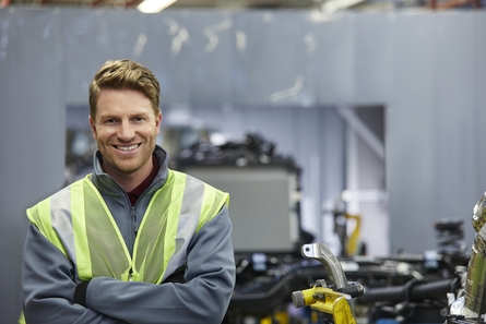 Mechanical engineer wearing jacket and work vest standing with arms folded in workshop