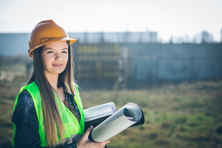 Civil engineer wearing helmet and vest standing next to construction site